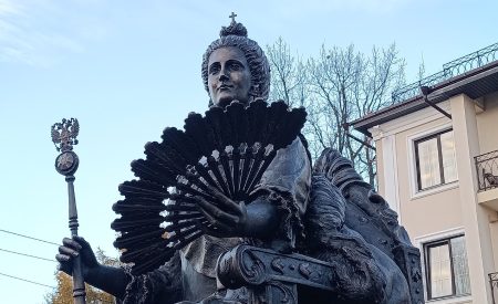 Скульптура Екатерины изображает властную женщину, сидящую на троне с веером в рукею